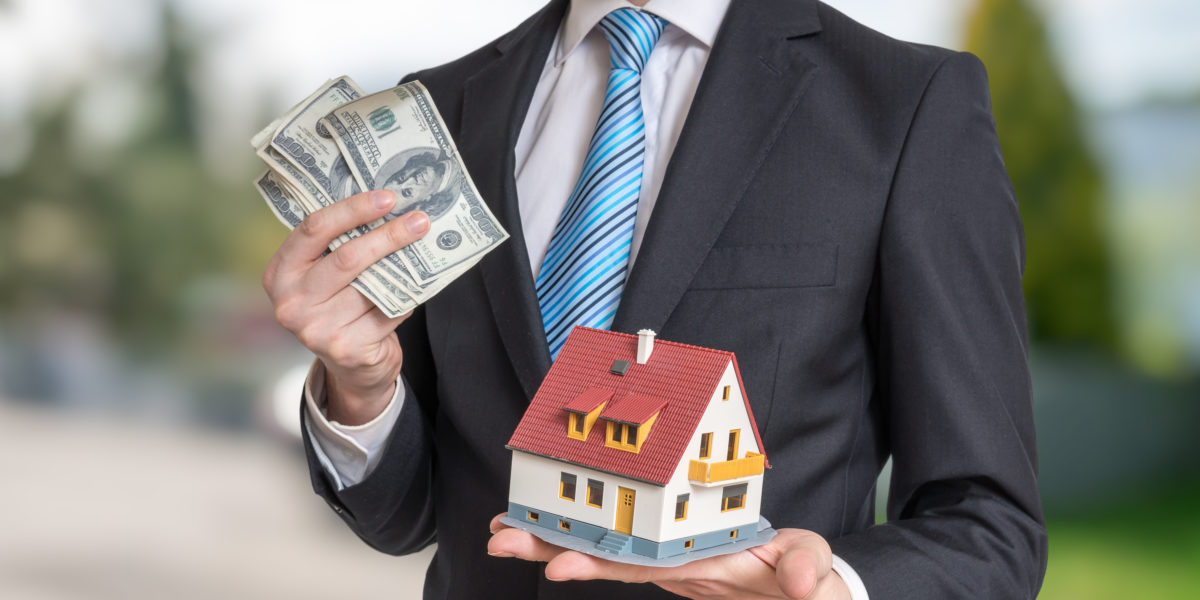 Real estate agent is holding small house and money in hands.